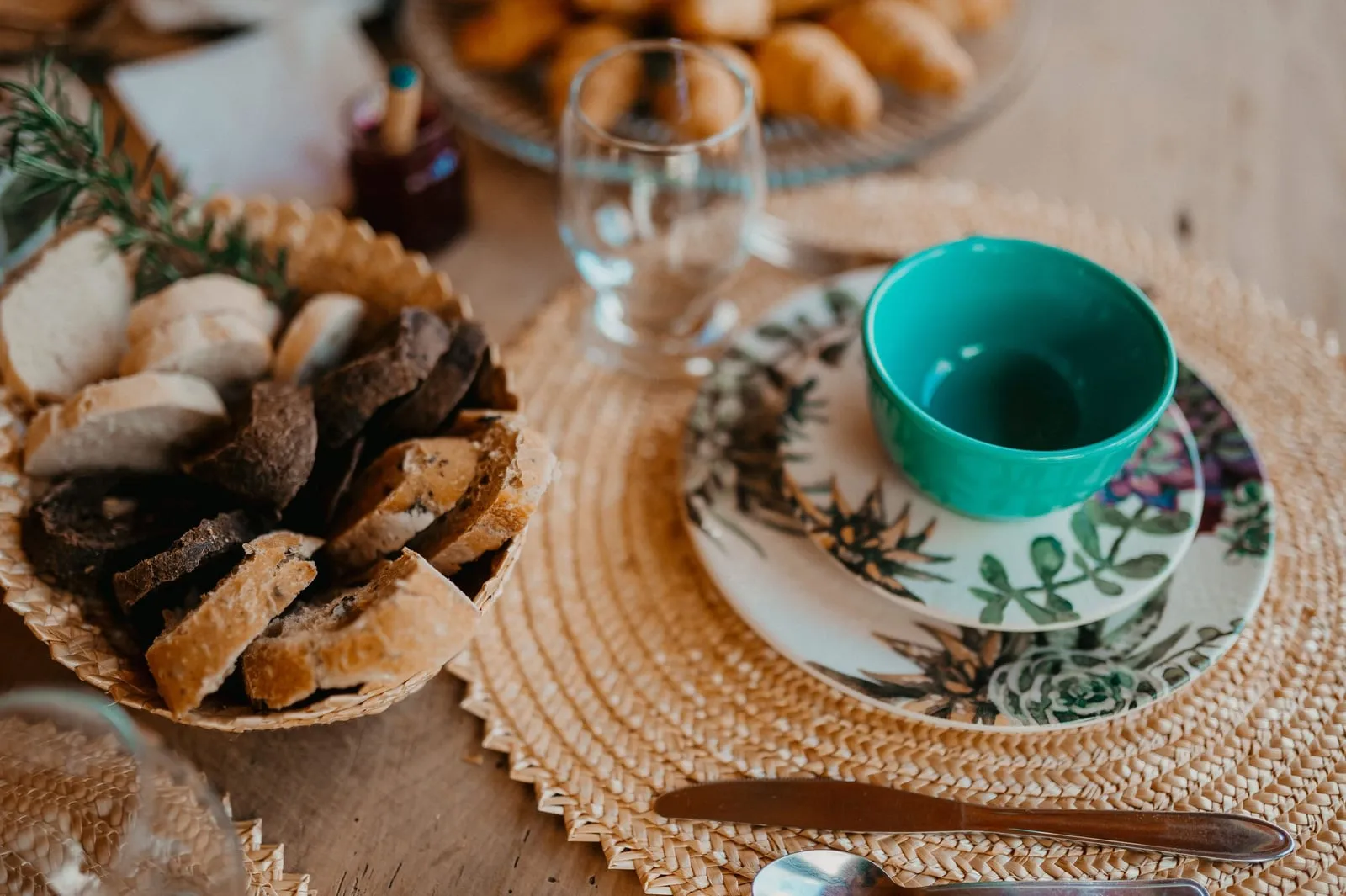 Mesa de café da manhã com pães, croissants e louça florida